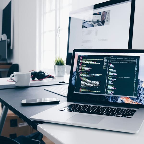 A MacBook with lines of code on its screen on a busy desk
